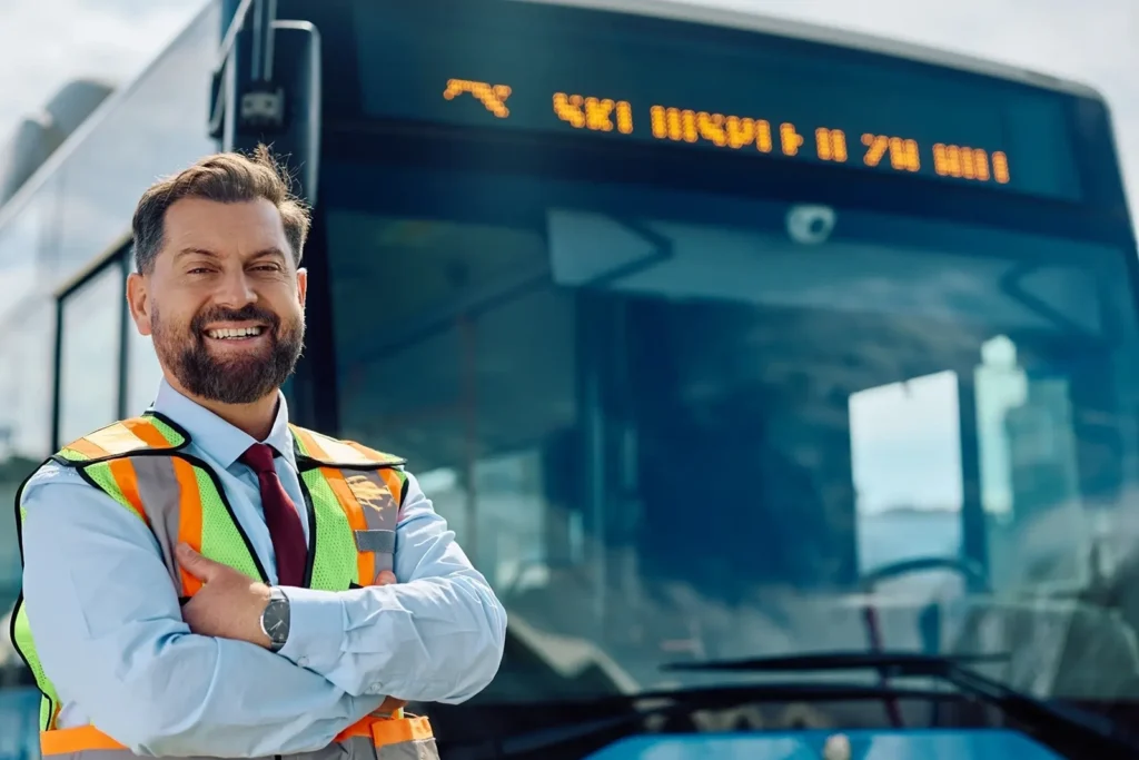Smiling transport supervisor standing before city bus at Belfast Private GP in Belfast