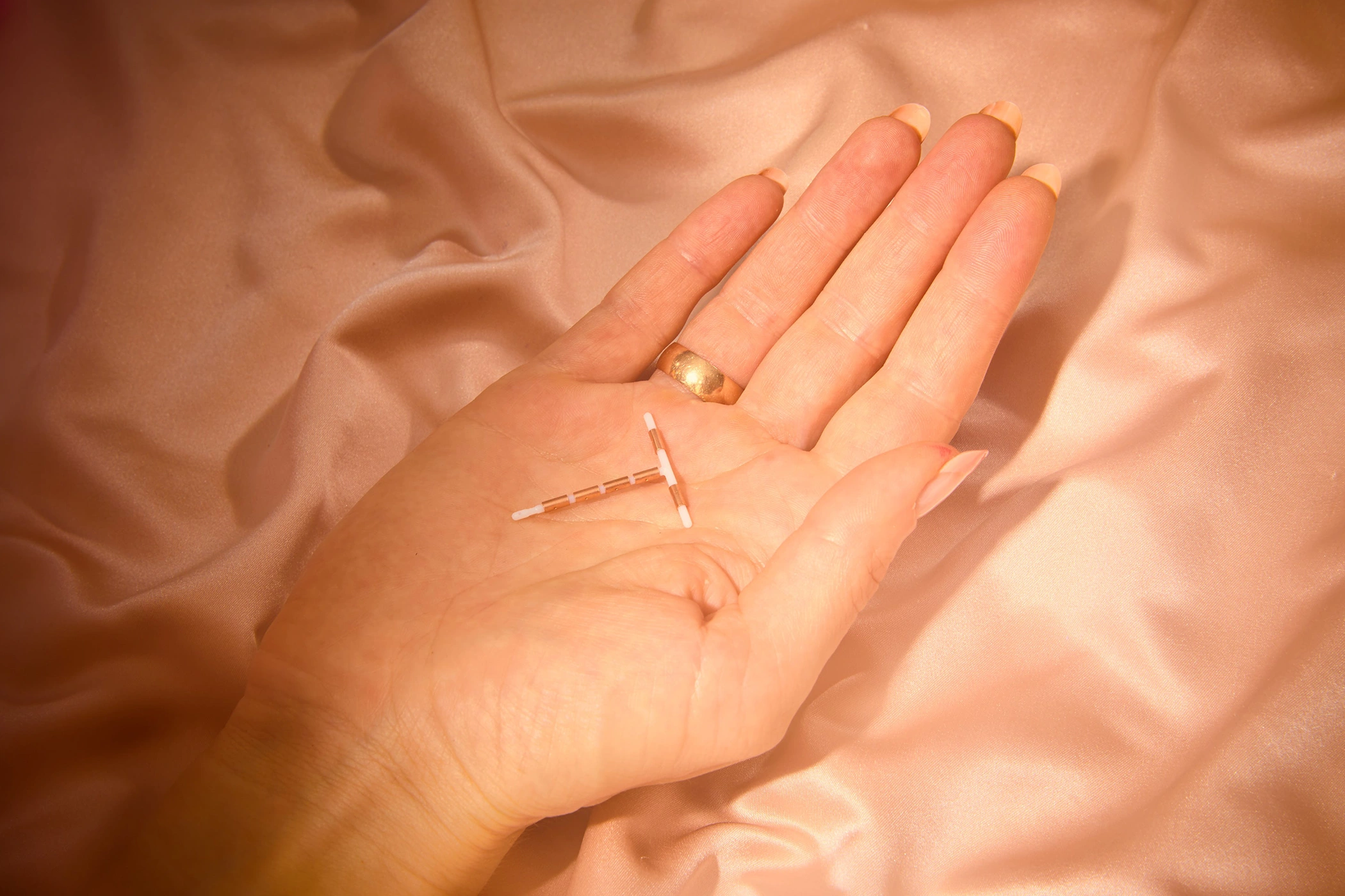 Hand holding intrauterine device on satin fabric at Belfast Private GP in Belfast