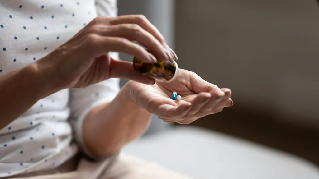 Hands pouring pills from bottle into palm.